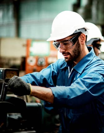 Engineer operating industrial machinery in workshop wearing safety helmet and gloves – THG Engineering Singapore